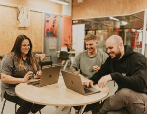 Three people working together around a table with open laptops