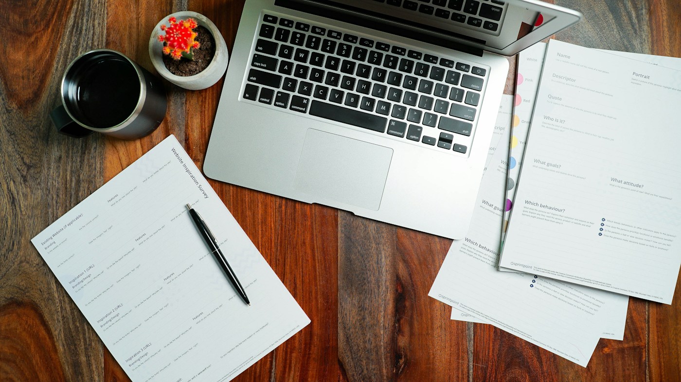 A laptop and planning documents on a wooden desk