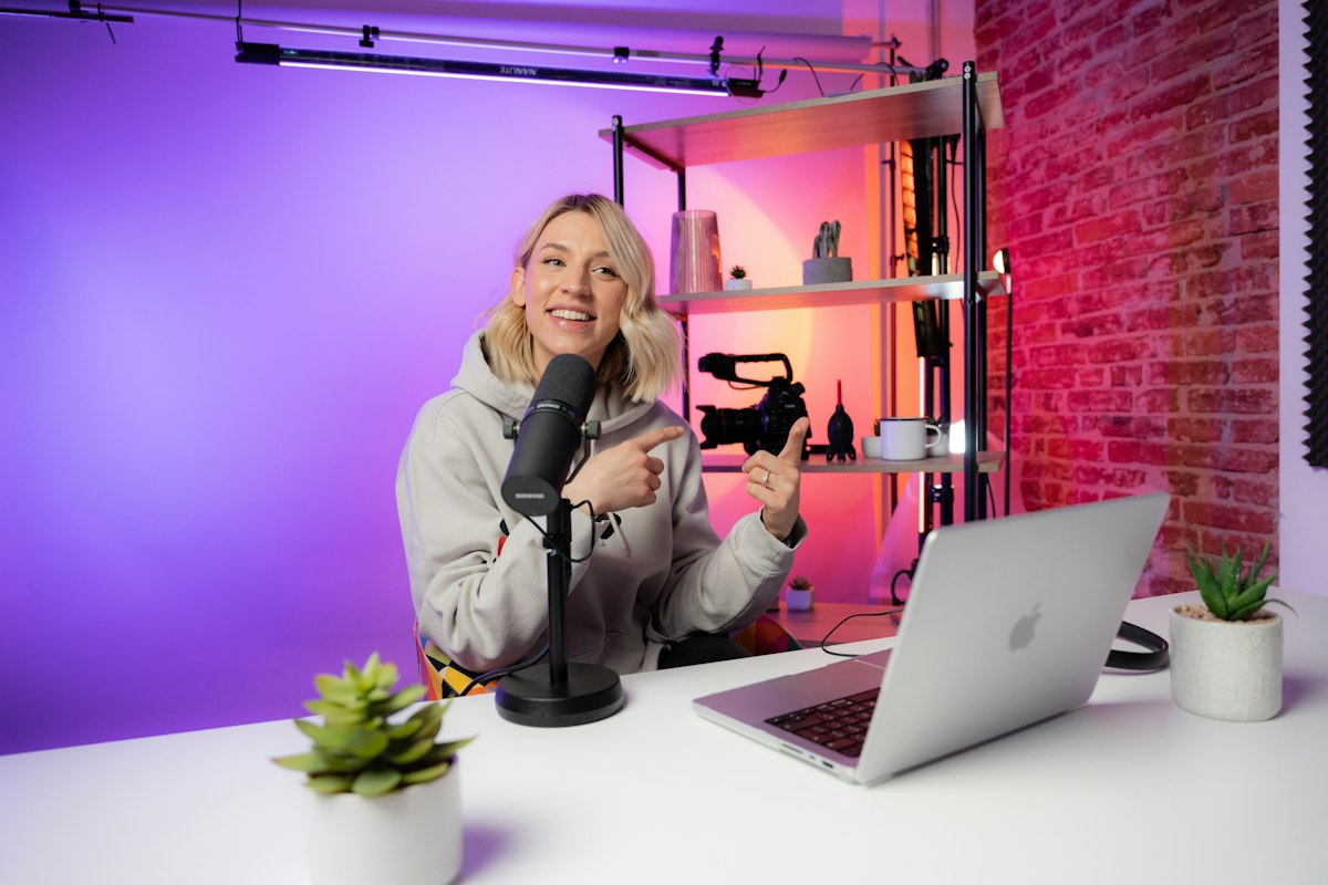 Creator at a desk with a microphone, laptop and video camera in a lit studio.