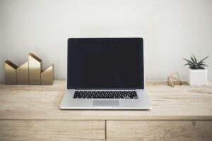 Laptop on a wooden desk beside a plant and stationery